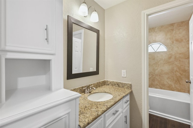 bathroom with bathtub / shower combination, vanity, and a textured wall