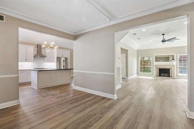 unfurnished living room with crown molding, ceiling fan with notable chandelier, light wood-style flooring, visible vents, and baseboards