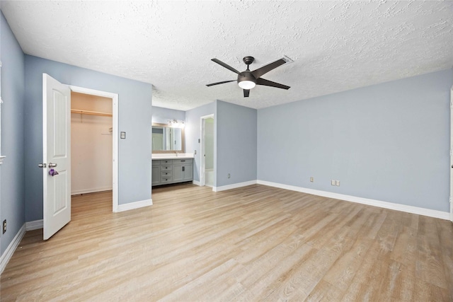 unfurnished bedroom with a textured ceiling, a closet, a spacious closet, light wood finished floors, and baseboards