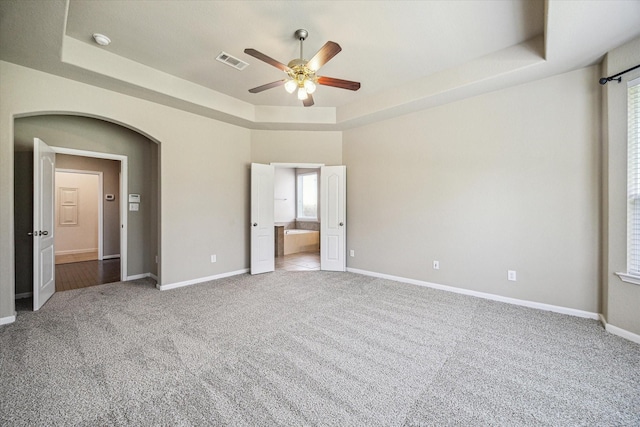 unfurnished bedroom with carpet floors, a tray ceiling, visible vents, and baseboards