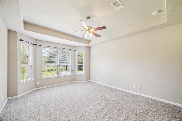 carpeted empty room featuring a raised ceiling, visible vents, baseboards, and ceiling fan