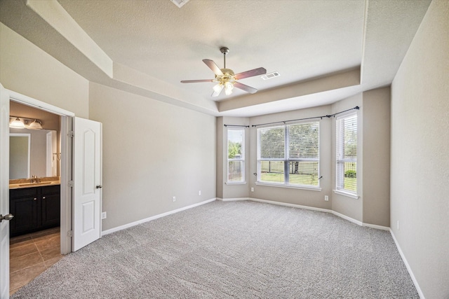 interior space with a raised ceiling, visible vents, a ceiling fan, and light colored carpet