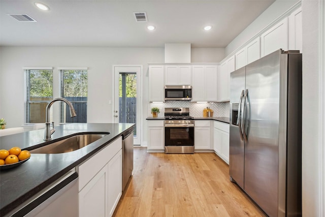 kitchen featuring tasteful backsplash, dark countertops, visible vents, stainless steel appliances, and a sink
