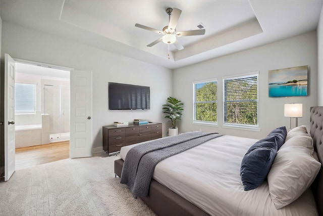 bedroom with visible vents, a ceiling fan, a tray ceiling, ensuite bath, and light carpet