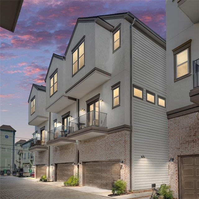 view of front of home with an attached garage, a balcony, brick siding, and stucco siding