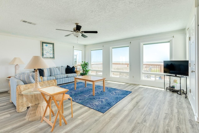 living area with wood finished floors, healthy amount of natural light, ceiling fan, a textured ceiling, and baseboards