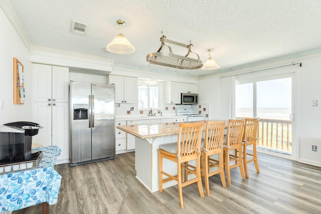 kitchen featuring stainless steel appliances, a breakfast bar area, white cabinetry, light wood-style flooring, and a textured ceiling