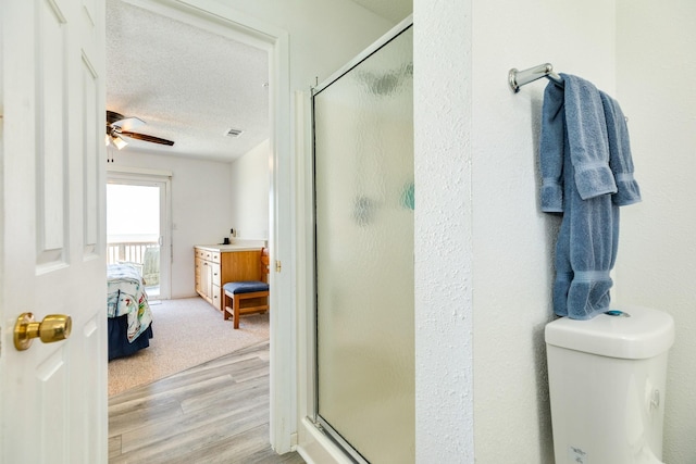 bathroom with a stall shower, wood finished floors, a ceiling fan, connected bathroom, and toilet