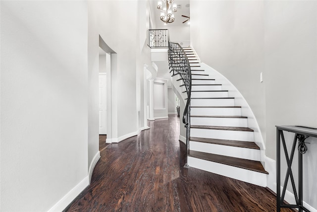 stairs featuring a high ceiling, wood finished floors, baseboards, and a chandelier