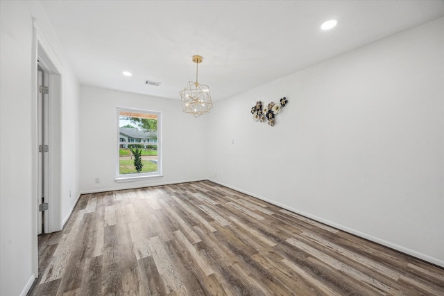unfurnished room featuring baseboards, visible vents, wood finished floors, and an inviting chandelier