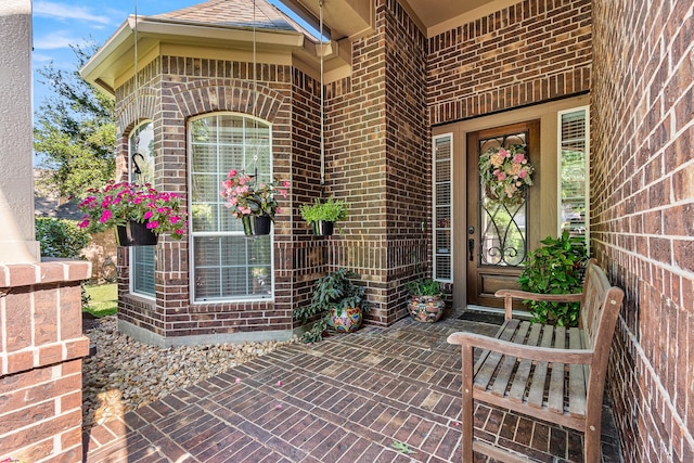 doorway to property featuring a porch and brick siding