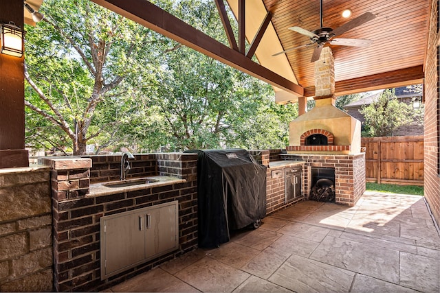 view of patio with fence, a ceiling fan, area for grilling, an outdoor brick fireplace, and a sink