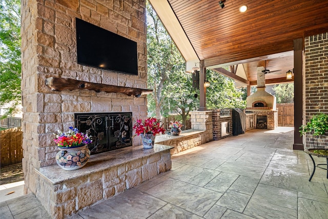 view of patio with fence, ceiling fan, area for grilling, and an outdoor stone fireplace