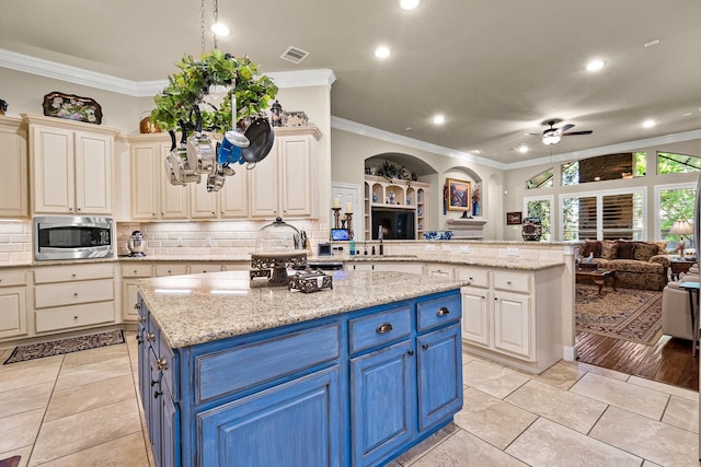 2469 S Bramlet Dr, Conroe, TX 77304 - kitchen featuring blue cabinetry, open floor plan, a ceiling fan, stainless steel microwave, and ornamental molding