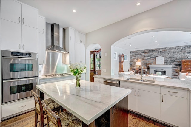 609 Reinicke St, Houston, TX 77007 - kitchen with light wood-type flooring, wall chimney exhaust hood, stainless steel appliances, arched walkways, and a sink