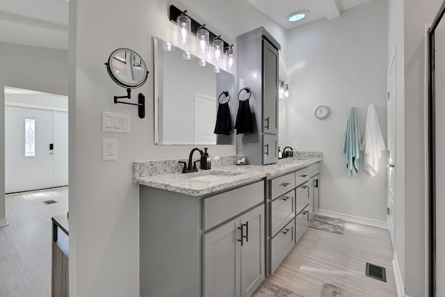 bathroom with visible vents, baseboards, a sink, double vanity, and wood finished floors