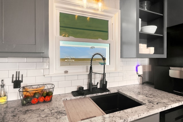 kitchen with a sink, gray cabinetry, backsplash, and light stone countertops
