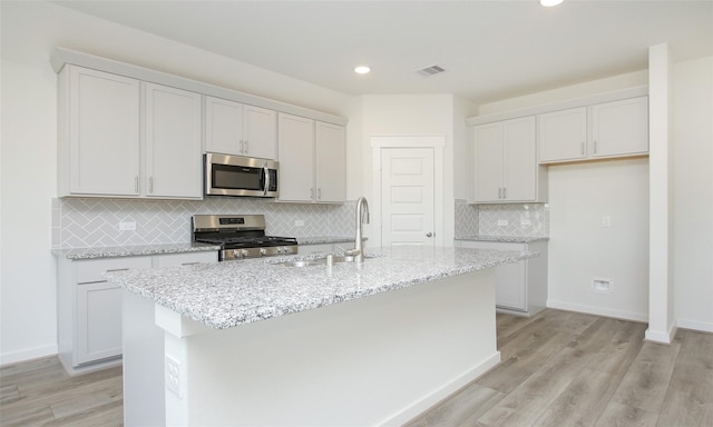 kitchen featuring light wood-style flooring, visible vents, a center island with sink, appliances with stainless steel finishes, and a sink