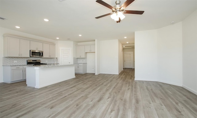 kitchen featuring stainless steel appliances, tasteful backsplash, light wood-style flooring, and a ceiling fan