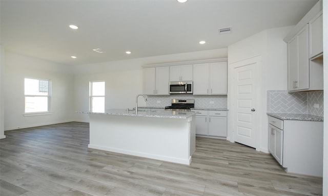 kitchen with light stone countertops, light wood-type flooring, a sink, stainless steel appliances, and backsplash