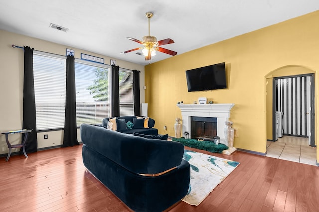 living area with visible vents, a ceiling fan, a glass covered fireplace, and hardwood / wood-style flooring