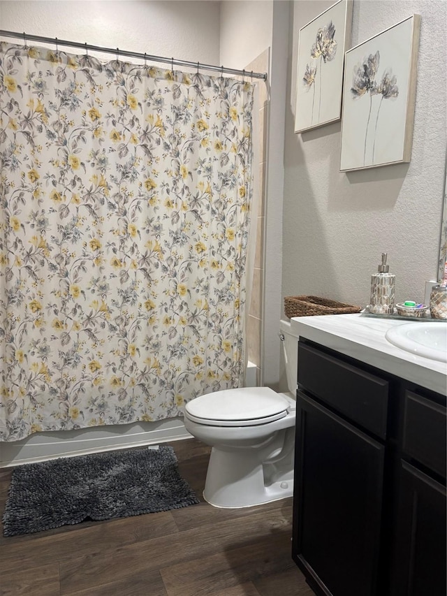 full bath with vanity, shower / bath combo with shower curtain, toilet, a textured wall, and wood finished floors