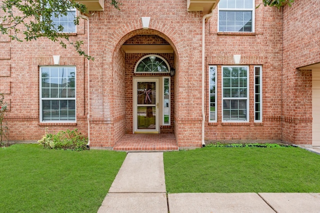 view of exterior entry featuring brick siding and a lawn