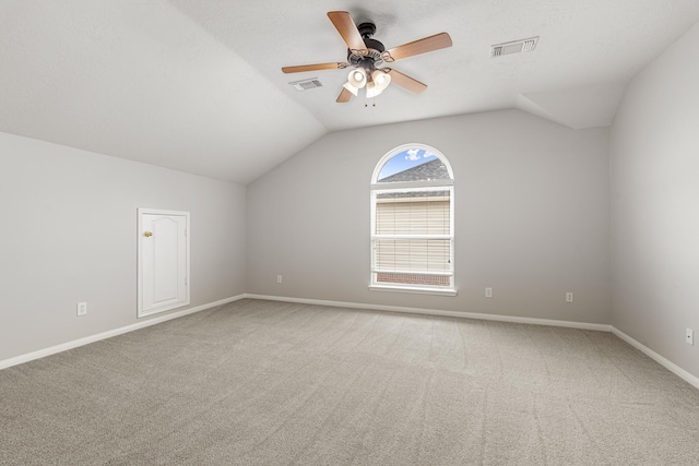 carpeted empty room with visible vents, a ceiling fan, and vaulted ceiling