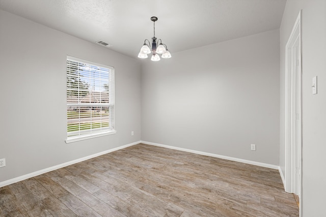 spare room featuring visible vents, baseboards, a notable chandelier, and light wood-style floors