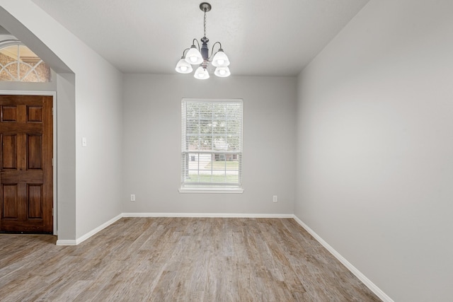 unfurnished room featuring light wood-style floors, baseboards, and an inviting chandelier