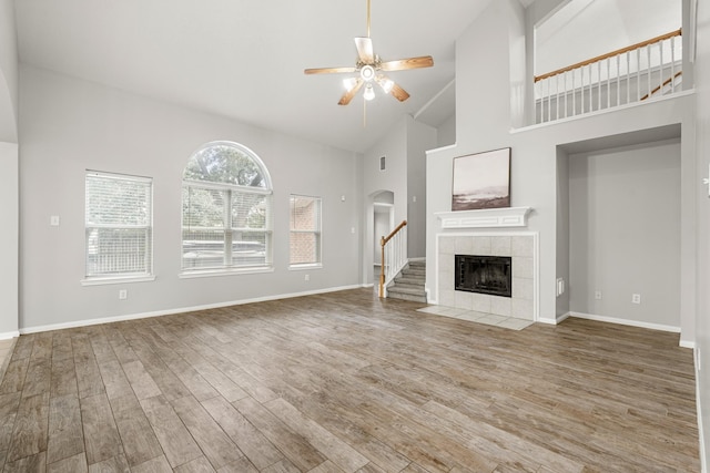 unfurnished living room featuring baseboards, a ceiling fan, high vaulted ceiling, a tile fireplace, and wood finished floors