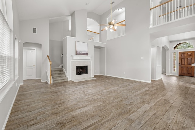unfurnished living room featuring a fireplace, a ceiling fan, visible vents, arched walkways, and wood finished floors