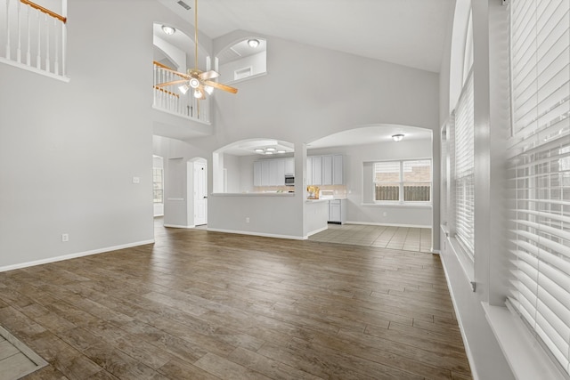 unfurnished living room with baseboards, dark wood finished floors, high vaulted ceiling, arched walkways, and ceiling fan