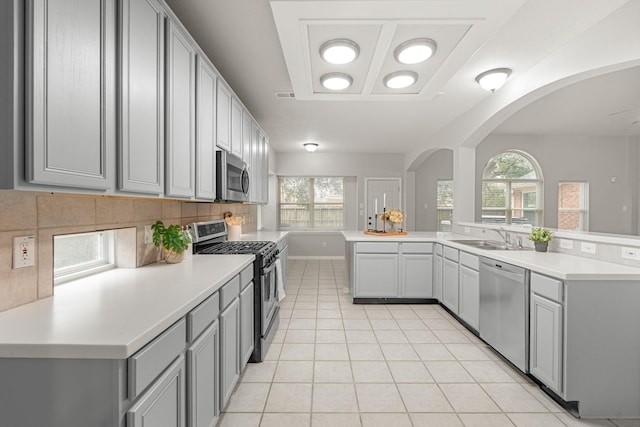 kitchen with gray cabinets, appliances with stainless steel finishes, a sink, light countertops, and decorative backsplash