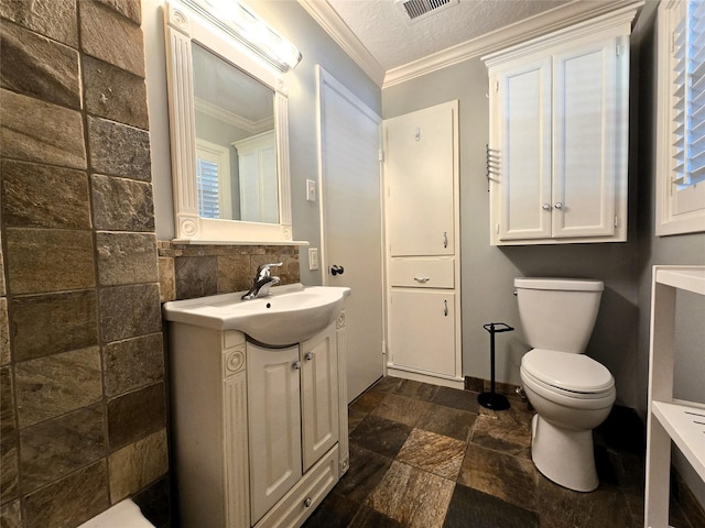 bathroom with crown molding, vanity, toilet, visible vents, and stone tile flooring