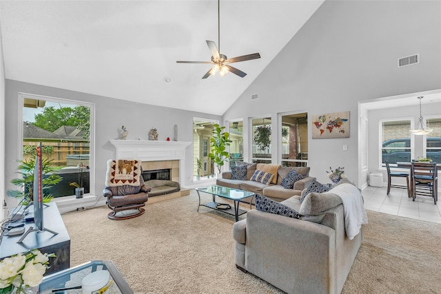 carpeted living area with ceiling fan, high vaulted ceiling, plenty of natural light, and a tiled fireplace