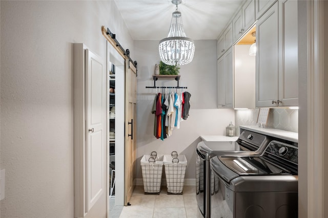 washroom featuring washing machine and clothes dryer, cabinet space, a barn door, light tile patterned floors, and a notable chandelier