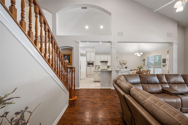 living area featuring light wood finished floors, high vaulted ceiling, a chandelier, baseboards, and stairway