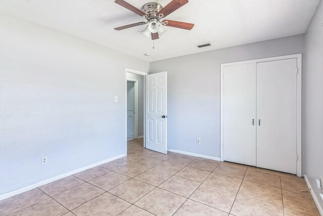 unfurnished bedroom featuring a textured ceiling, a closet, light tile patterned flooring, and baseboards