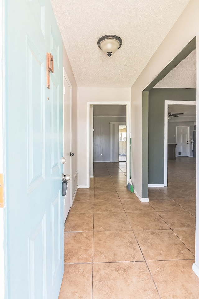 hall with light tile patterned floors, visible vents, a textured ceiling, and baseboards