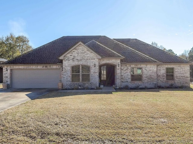 french country inspired facade with brick siding, a front yard, an attached garage, and concrete driveway