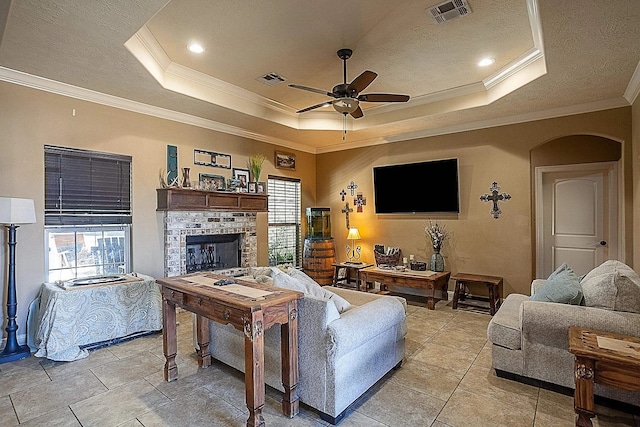 living area featuring ornamental molding, a fireplace, a ceiling fan, visible vents, and a tray ceiling