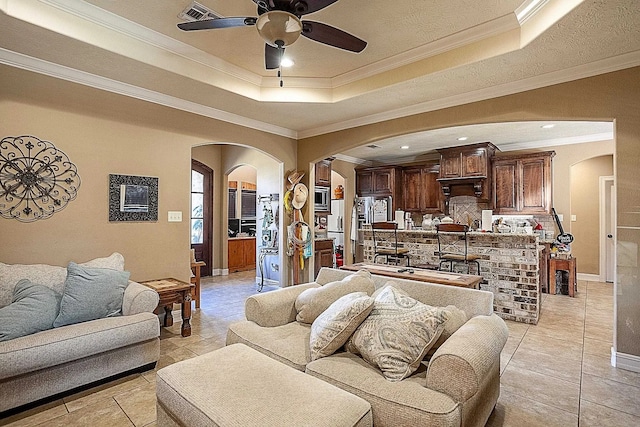 living area with a raised ceiling, arched walkways, and a ceiling fan