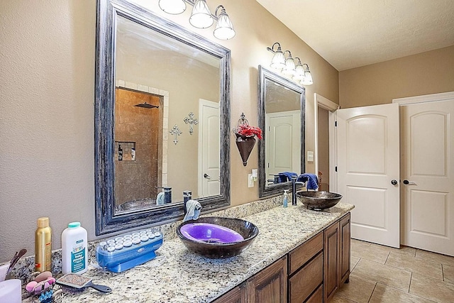 full bath featuring tiled shower, double vanity, a sink, and tile patterned flooring