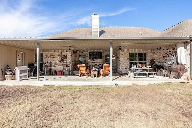 rear view of property featuring a chimney, a patio area, a ceiling fan, and brick siding