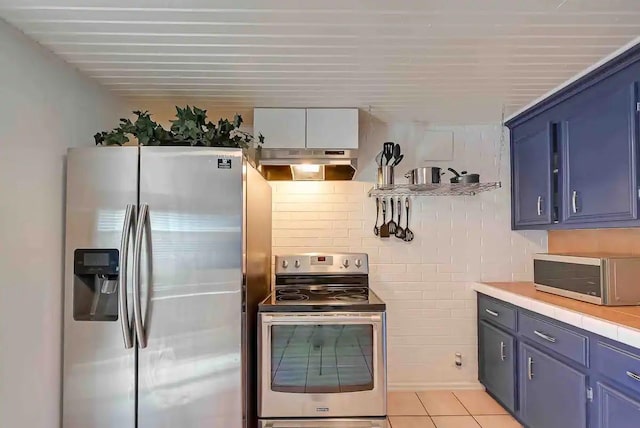 1265 Du Barry Ln, Houston, TX 77018 - kitchen with light tile patterned floors, appliances with stainless steel finishes, blue cabinets, light countertops, and under cabinet range hood