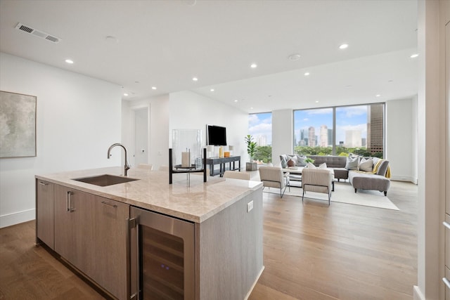 kitchen with a sink, an island with sink, light wood finished floors, wine cooler, and visible vents