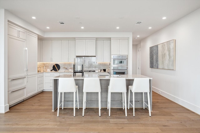 kitchen featuring stainless steel double oven, visible vents, recessed lighting, and an island with sink
