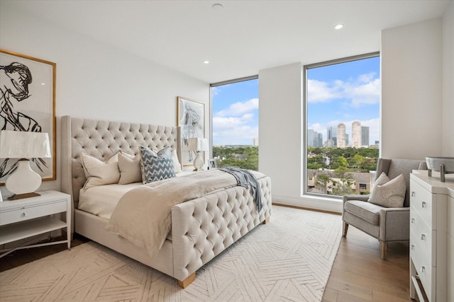 bedroom with a city view, light wood-style flooring, expansive windows, and recessed lighting