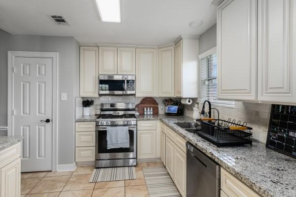 kitchen with tasteful backsplash, light tile patterned floors, visible vents, appliances with stainless steel finishes, and a sink
